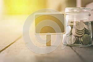 Wooden signage and coin in jar .fade color effect wooden background with light effect