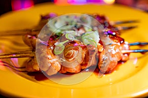 Wooden skewers with pieces of chicken fillet in teriyaki sauce from the grill served at yakitori restaurant in Milan, Italy