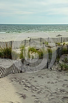 A wooden slated sand fence is partly buried in an ocean beach dune.