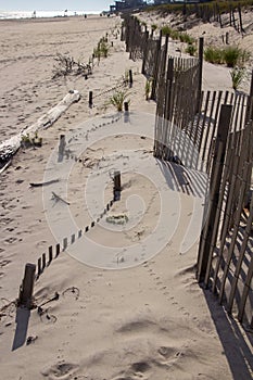 A wooden slated sand fence is partly buried in an ocean beach dune.