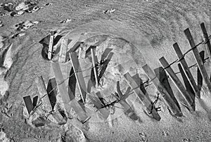 A wooden slated sand fence is partly buried in an ocean beach dune