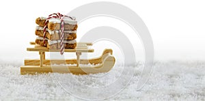 wooden sled in the snow with cinnamon stars, traditional christmas cookies, background with copy space fades to white