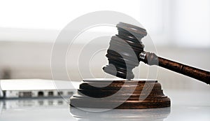 Wooden sledge gavel on a modern table. Modern law office. Books and laptop in the background.