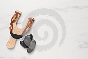 Wooden slingshot with stones on white marble background, flat lay. Space for text