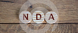 Wooden small circles with letters NDA on wood background. Concept image