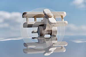 Wooden small toy light aircraft biplane on glossy reflective surface over background of cloudy sky.