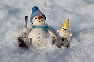 Wooden snowman and small snowman sledding in the snow