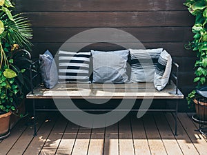 Wooden sofa with pillows between green tropical trees in terra cotta pots on wooden wall background