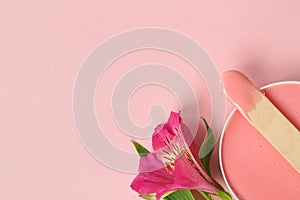 Wooden spatula, hot depilatory wax and flower on light pink background, flat lay. Space for text