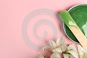 Wooden spatula, hot depilatory wax and flowers on light pink background, flat lay. Space for text