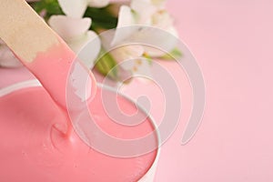 Wooden spatula and hot depilatory wax on light pink background, closeup. Space for text