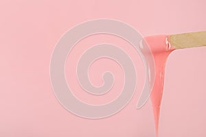 Wooden spatula with hot depilatory wax on pink background. Space for text