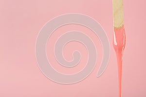 Wooden spatula with hot depilatory wax on pink background. Space for text