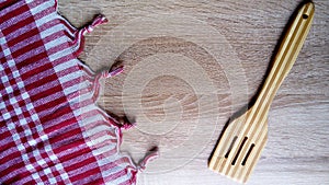 A wooden spatula for stirring cooked food. A kitchen tablecloth made of red-and-white checked fabric is on the right