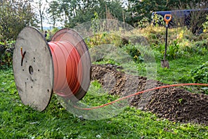 Wooden spool with fiber optic cable for fast internet ready to be laid in narrow trenches in the ground on a meadow,