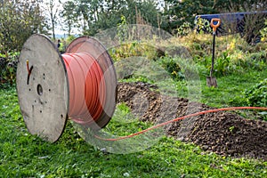 Wooden spool with fiber optic cable for fast internet ready to be laid in narrow trenches in the ground on a meadow, photo