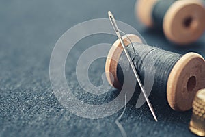 Wooden spools of blue thread and thimble on blue jeans cloth