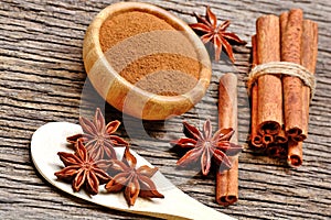 Wooden spoon with anise star and cinnamon powder with sticks on table