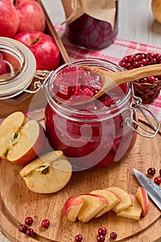 Wooden spoon with appetizing lingonberry and apple jam, jar of jam, fresh fruits and berries on light wooden table. Home canning