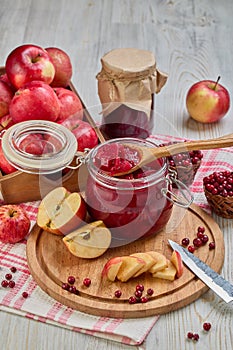 Wooden spoon with appetizing lingonberry and apple jam, jar of jam, fresh fruits and berries on light wooden table. Home canning