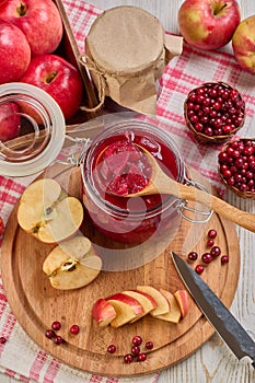 Wooden spoon with appetizing lingonberry and apple jam, jar of jam, fresh fruits and berries on light wooden table. Home canning