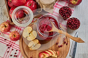 Wooden spoon with appetizing lingonberry and apple jam, jar of jam, fresh fruits and berries on light wooden table. Home canning