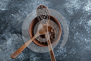 A wooden spoon of chocolate chips with clay bowl of coffee beans