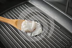 Wooden spoon with coconut oil in frying pan