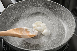 Wooden spoon with coconut oil in frying pan