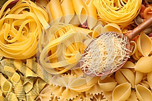 Wooden spoon and different types of pasta as background, top view