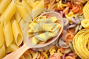 Wooden spoon and different types of pasta as background, top view