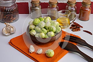 Wooden spoon and fork, various spices and oil near ripe brussels sprouts lies in a wooden bowl and on a table