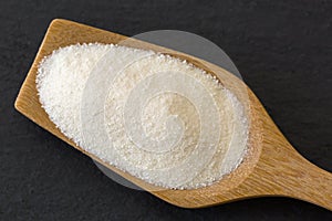 Wooden spoon full of dried white fine powder starch on dark stone.