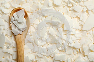 Wooden spoon on heap of soy wax flakes, top view. Homemade candle material