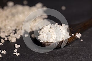 Wooden spoon holding  white sea salt crystals on a black slate cutting board