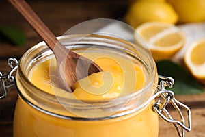 Wooden spoon in jar with lemon curd on table, closeup photo