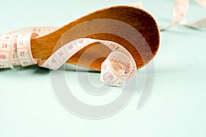 Wooden spoon with a measuring tape on a blue background, diet, healthy lifestyle.