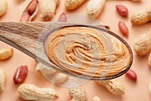 Wooden spoon with peanut butter. Peanuts lay on beige at the background. Top view