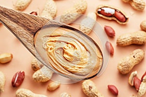 Wooden spoon with peanut butter. Peanuts lay on beige at the background. Top view