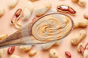 Wooden spoon with peanut butter. Peanuts lay on beige at the background. Top view