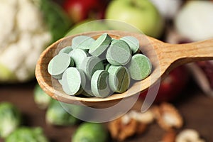 Wooden spoon of pills over table with foodstuff, closeup. Prebiotic supplements