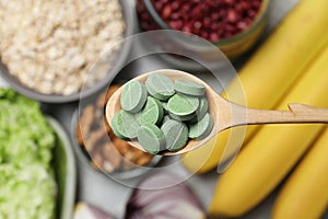 Wooden spoon of pills over table with foodstuff, top view. Prebiotic supplements