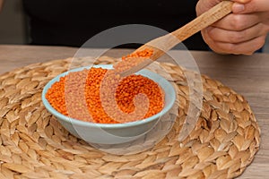 Wooden Spoon of Red Lentils Over Bowl. Scooping vibrant red lentils with a wooden spoon from a bowl