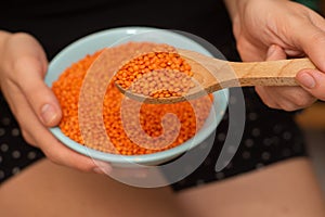 Wooden Spoon of Red Lentils Over Bowl. Scooping vibrant red lentils with a wooden spoon from a bowl