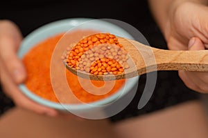 Wooden Spoon of Red Lentils Over Bowl. Scooping vibrant red lentils with a wooden spoon from a bowl