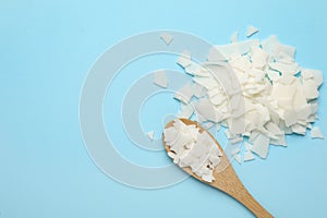 Wooden spoon and soy wax flakes on light blue background, flat lay with space for text. Homemade candle material