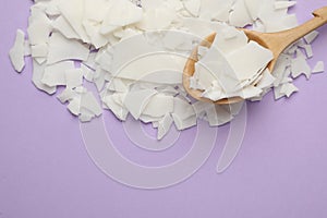 Wooden spoon and soy wax flakes on violet background, flat lay with space for text. Homemade candle material