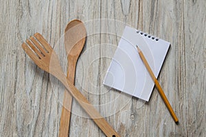 Wooden spoon and spatula with notebook and pencil on wooden background