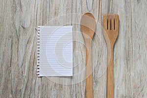 Wooden spoon and spatula with a sheet of paper on wooden background