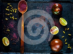 Wooden spoon with spice sumac, tomatoes of kumato and citrus fruit lime on vintage rusty metal background, ingredients for salads